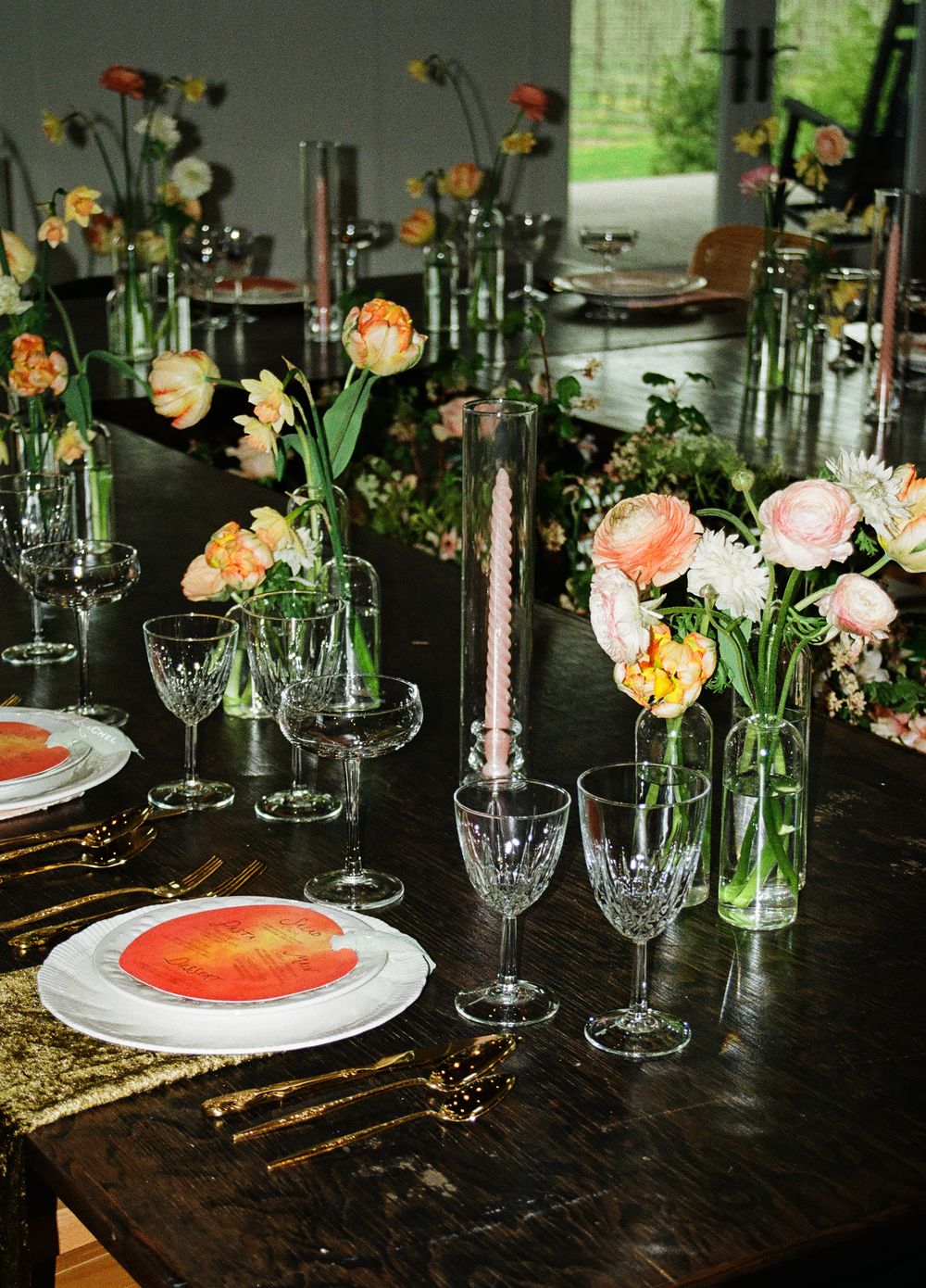 Elegant wedding table setting with crystal glasses, pink candles, and colorful floral arrangements on a dark wood table.