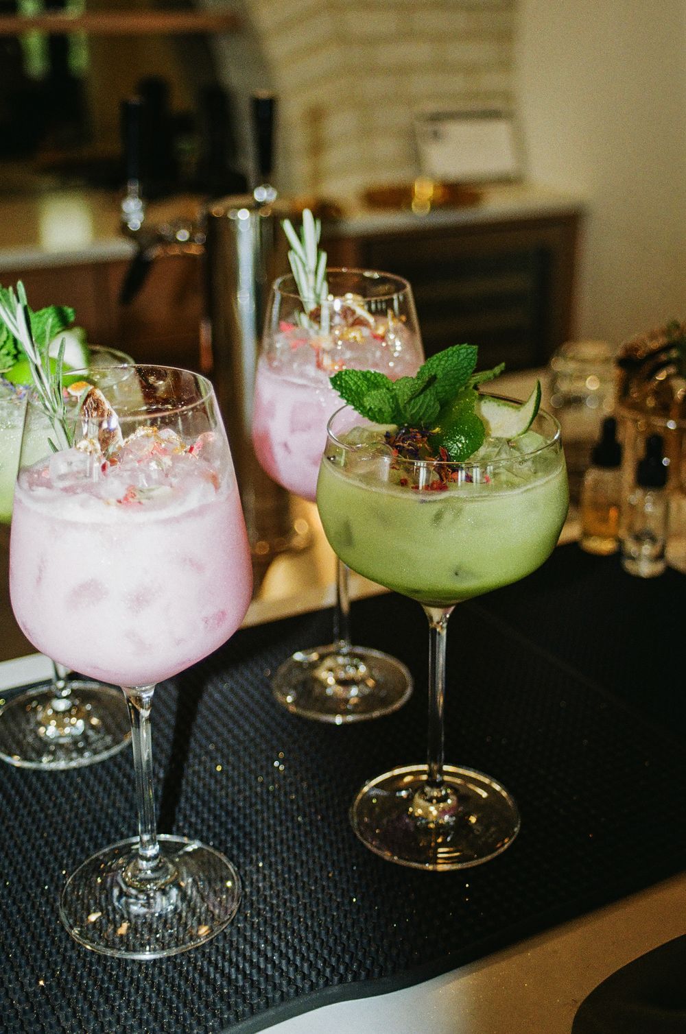 Elegant cocktails garnished with fresh mint and berries served in large wine glasses on a dark bar counter.