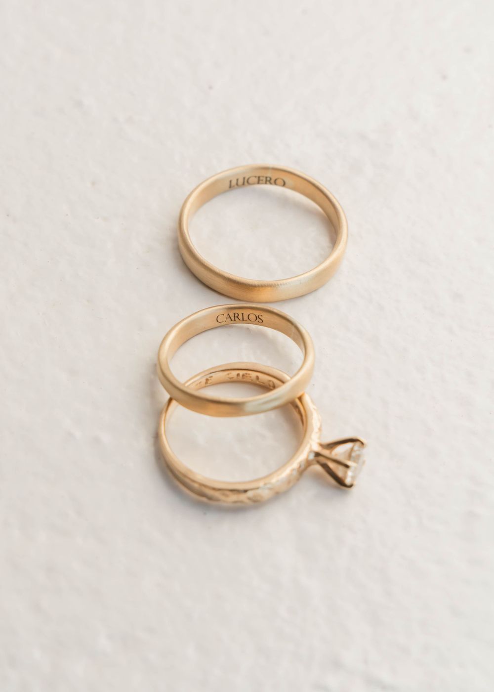 Gold wedding bands and engagement ring arranged on white surface.