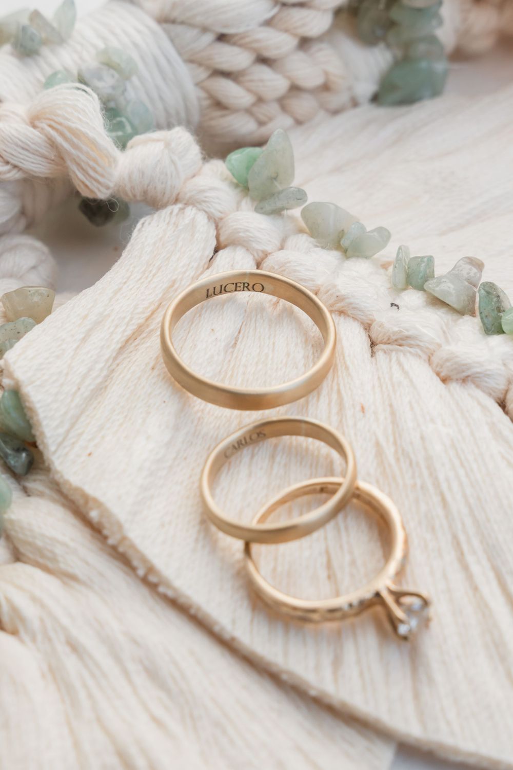 Gold wedding rings displayed on white macrame with delicate eucalyptus leaves.