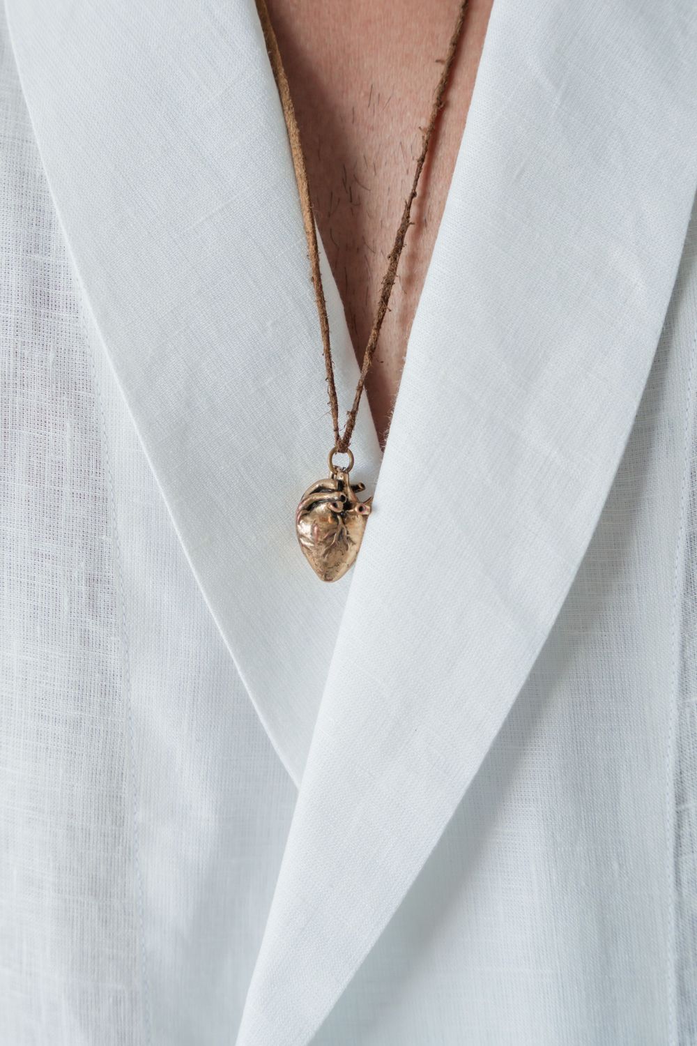 Gold anatomical heart necklace pendant against white linen lapel.