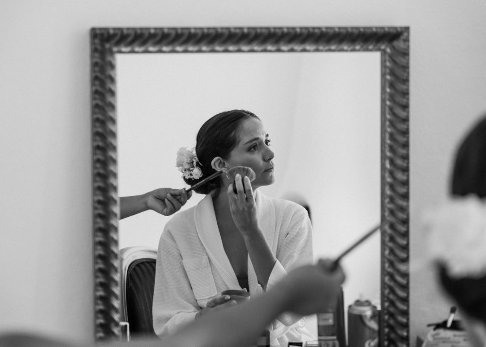 Black and white reflection of someone getting ready in an ornate framed mirror.