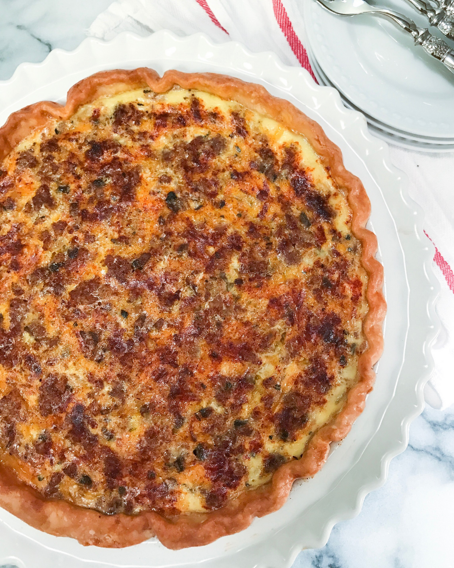 Golden brown quiche with melted cheese and meat filling in a scalloped pie dish.