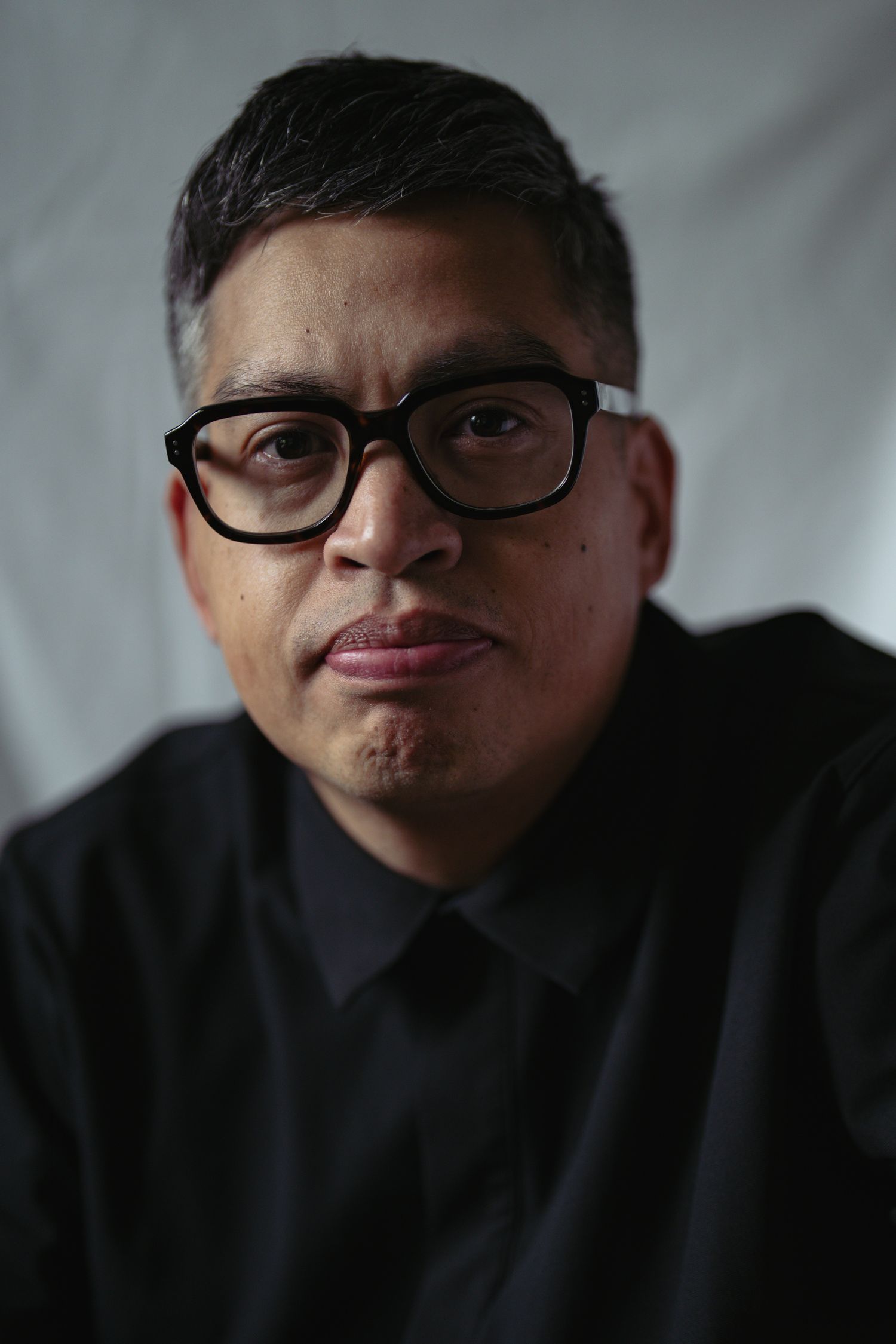 Close-up portrait of man with dark hair wearing black glasses and black shirt.