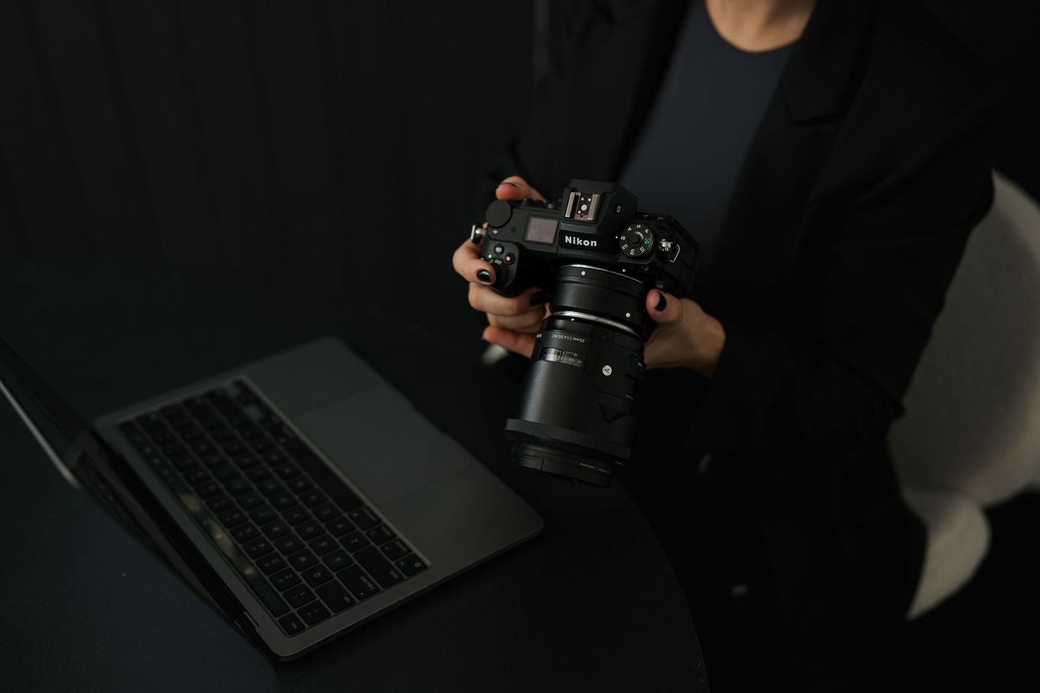 Professional camera and laptop setup on dark surface in moody lighting.