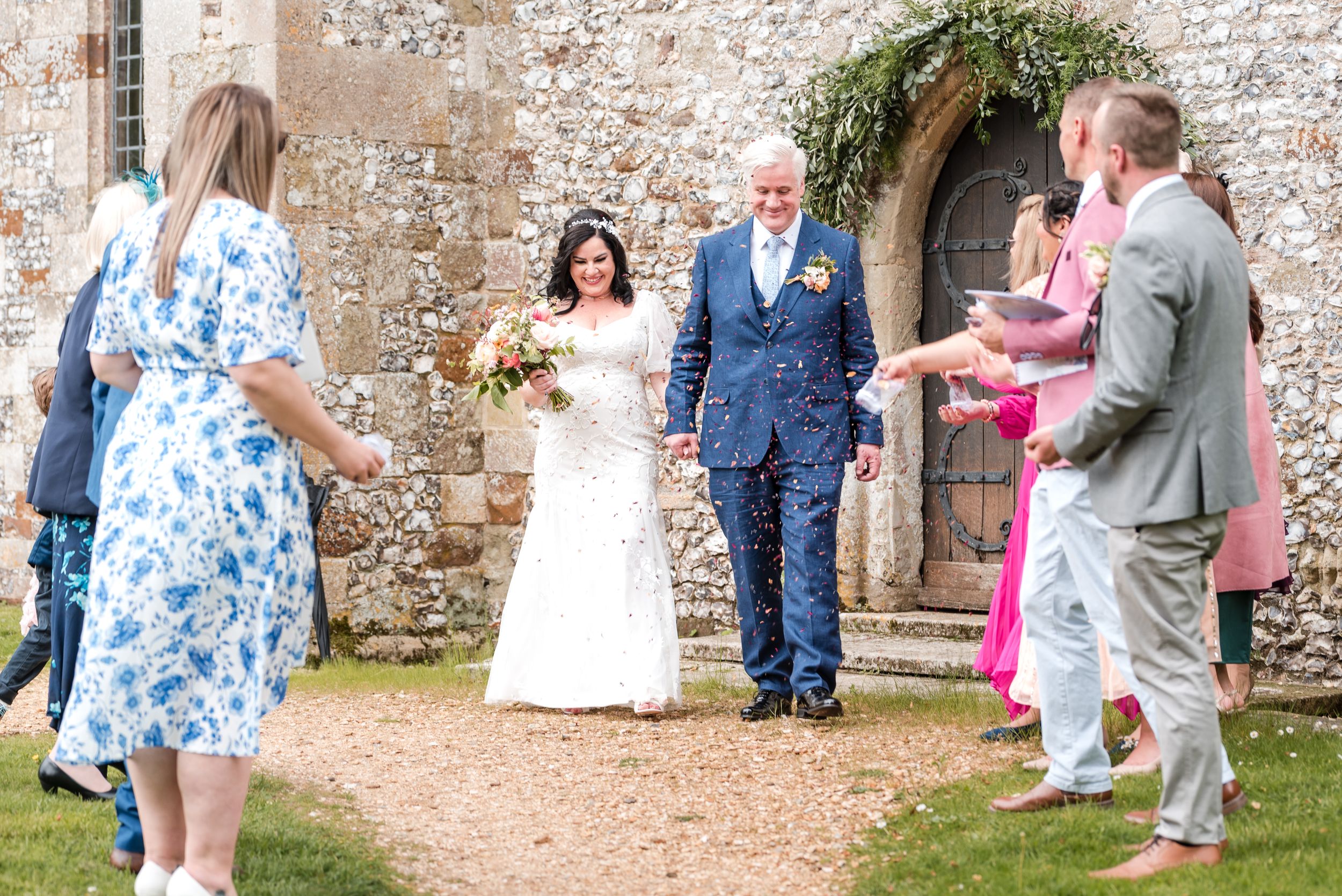 Wedding guests gather outside a stone church to celebrate with the newlyweds.