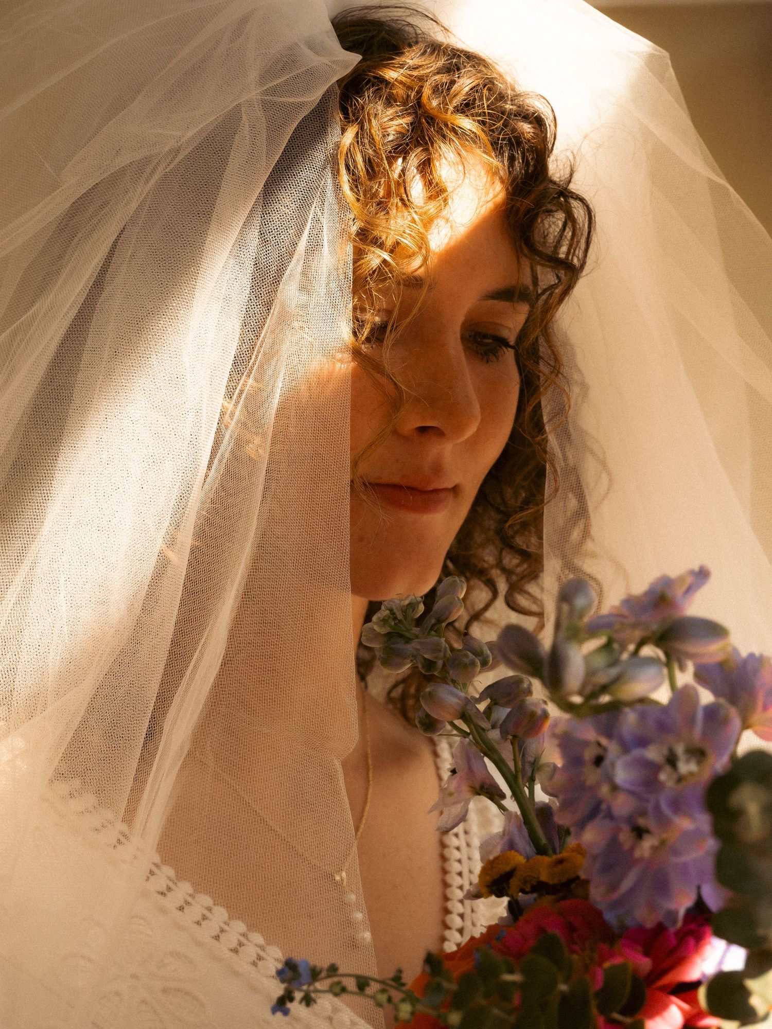 Sun-lit bridal portrait with delicate veil and purple floral bouquet.