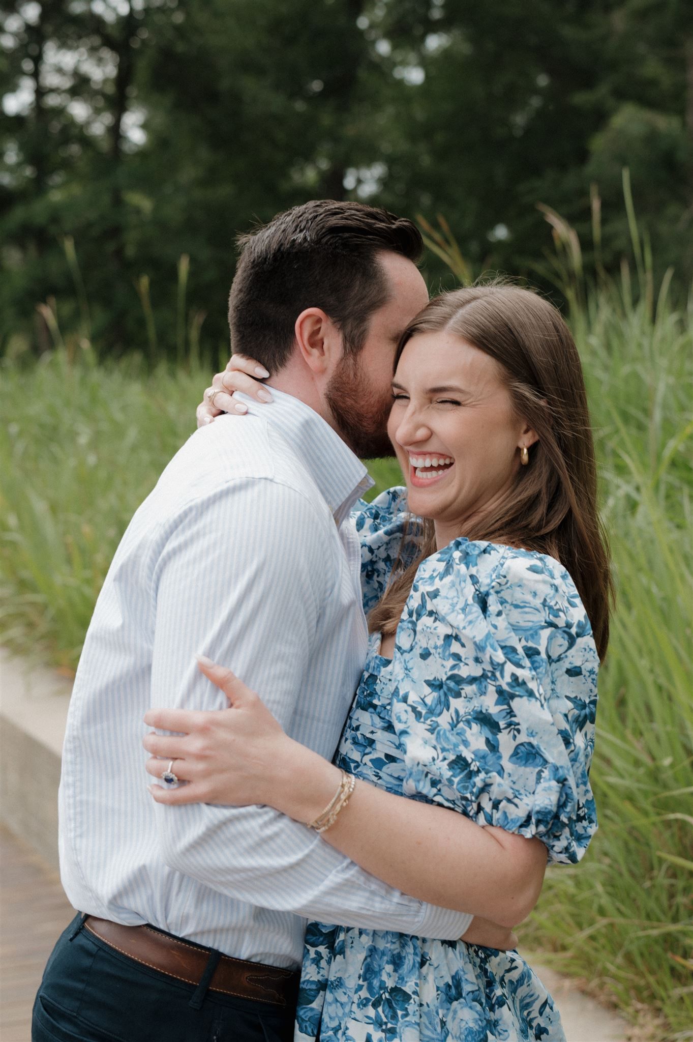 A joyful couple embraces on a wooden boardwalk surrounded by tall grass on a summer day.