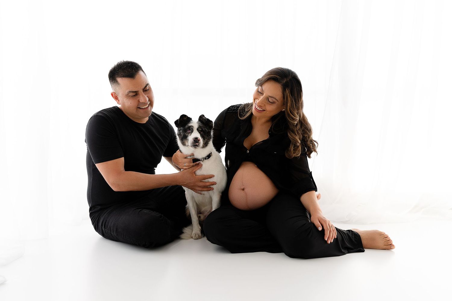 Expectant couple sits with their Border Collie dog during studio photoshoot.