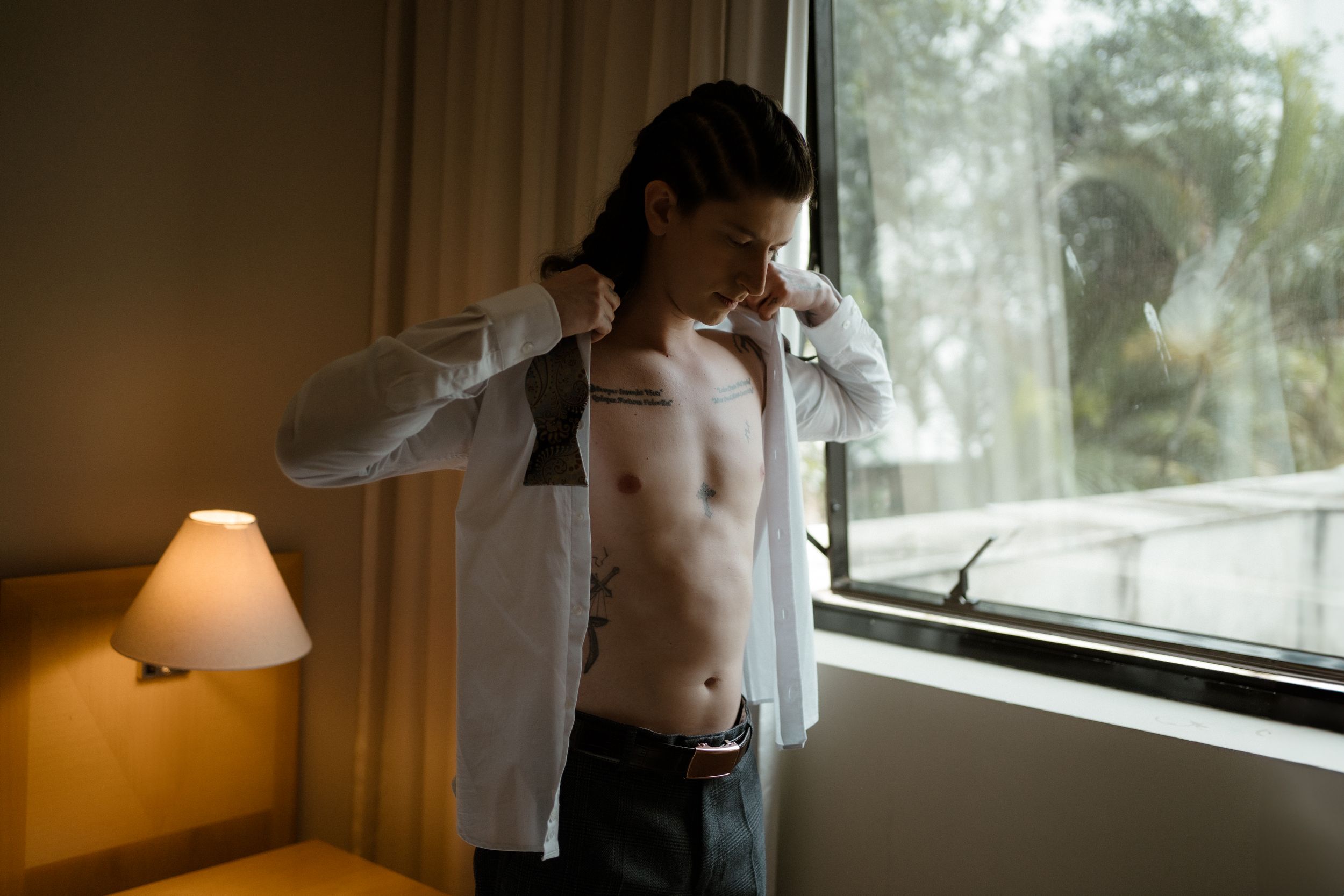 Morning light streams through window as white shirt is being put on.