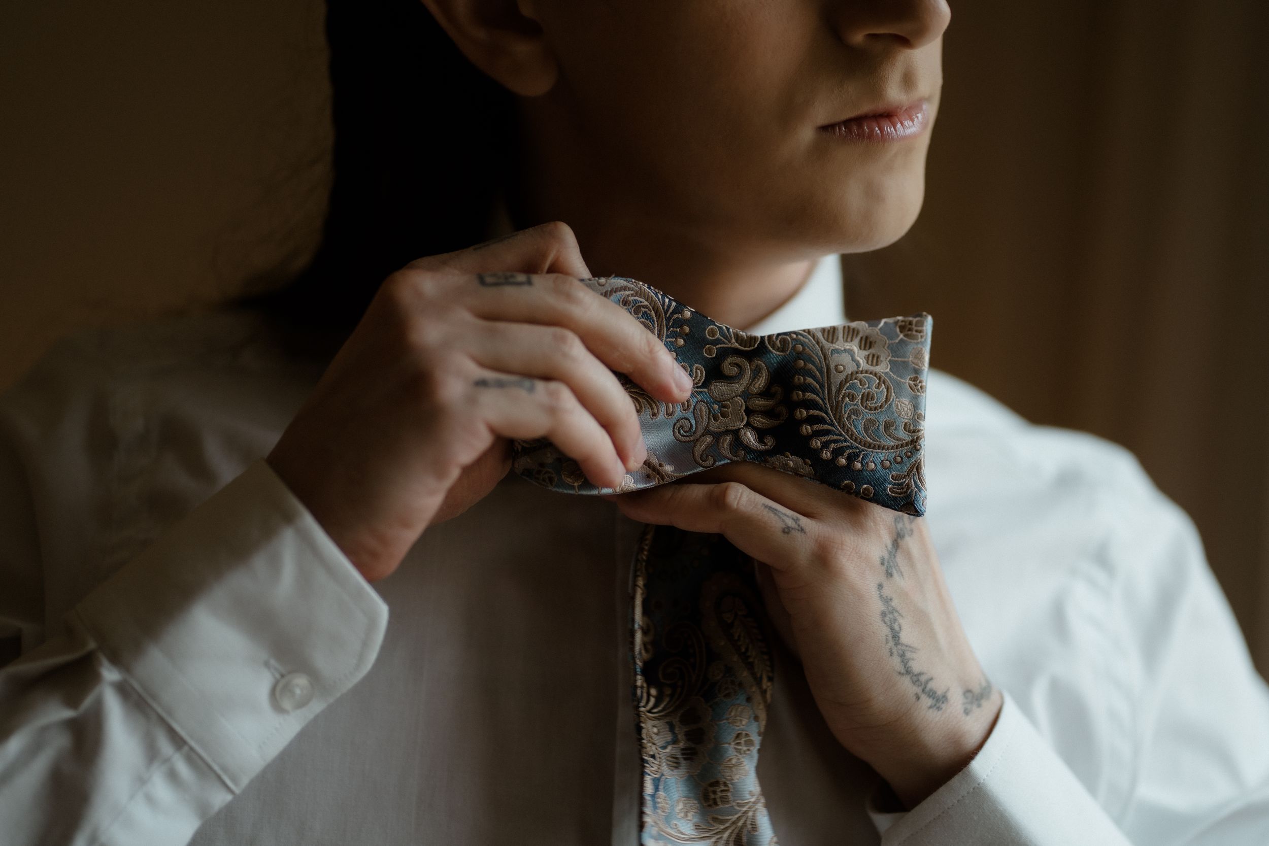 Details of formal attire being adjusted in moody lighting.