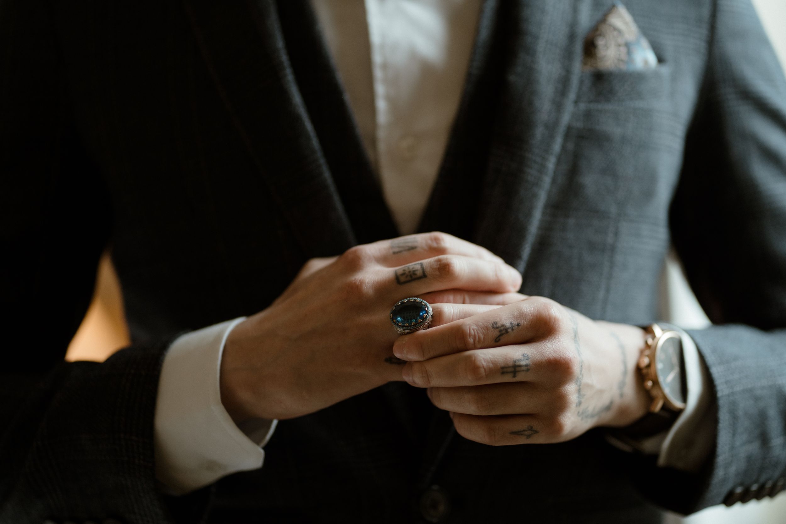 Close-up shots of hands wearing a silver ring and grey suit in dramatic lighting.