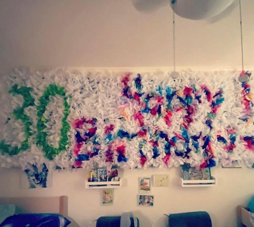 Colorful birthday party decoration spelled out in tissue paper pom-poms on a wall.