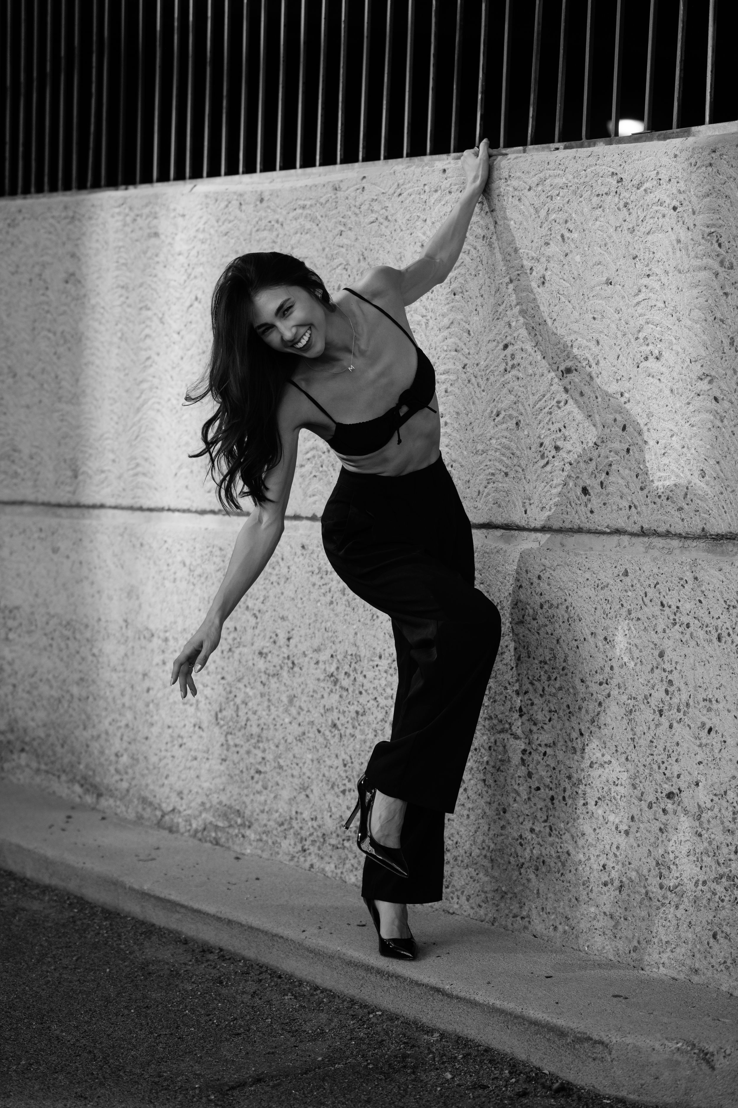 Black and white portrait of a model wearing a white tank top and light jeans in an artistic pose against dark background.