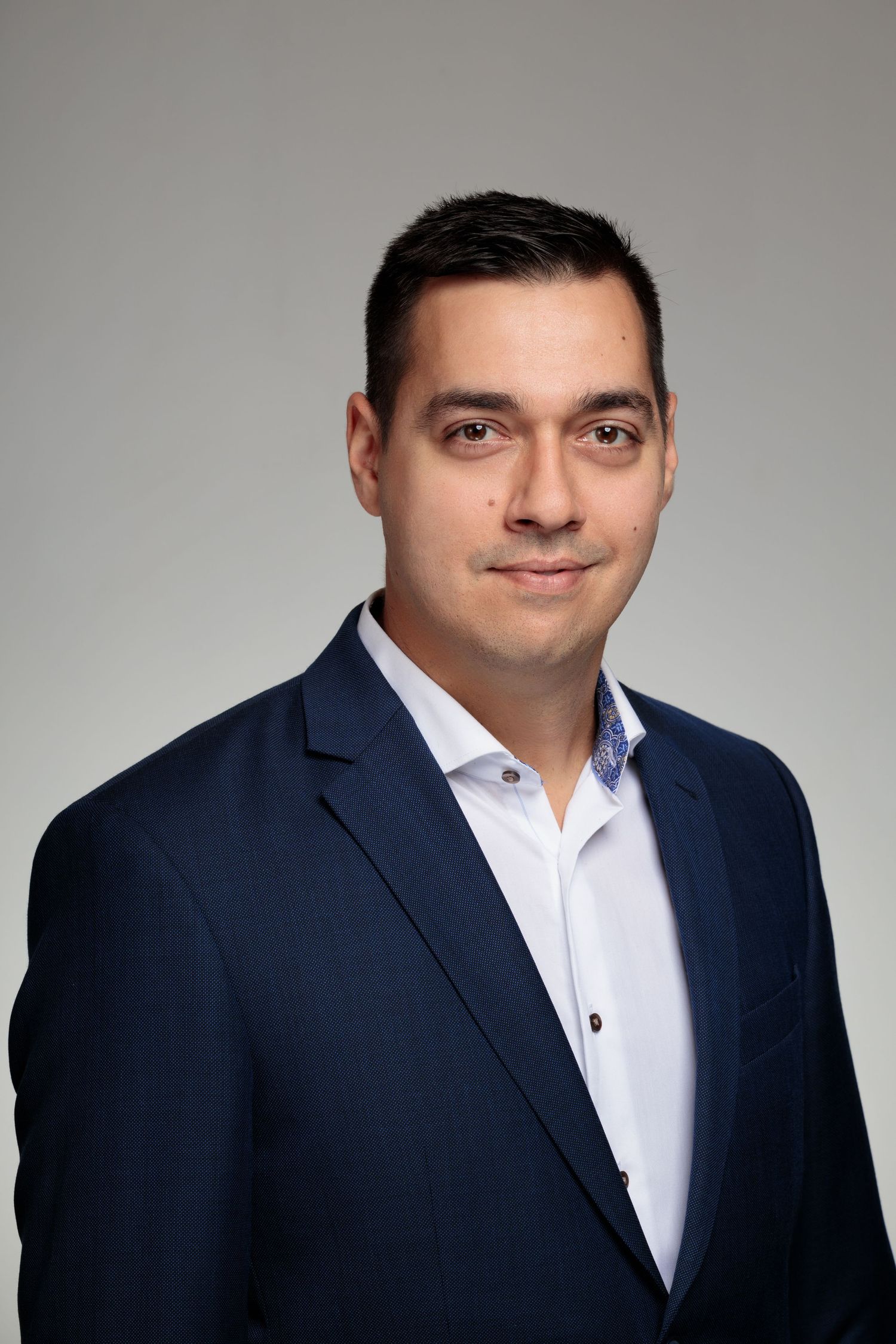 Professional headshot against grey background wearing navy suit and white shirt.