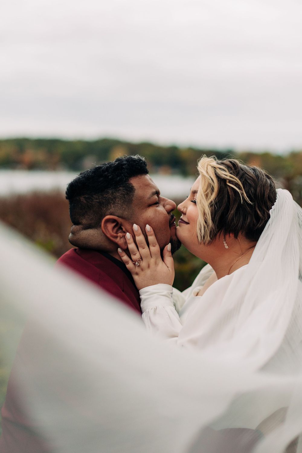 An intimate wedding moment captured against a misty autumn landscape with flowing white veil.