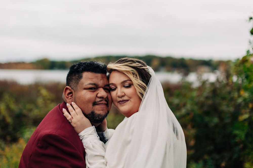 Candid wedding moment showing affectionate embrace against autumn lakeside scenery.