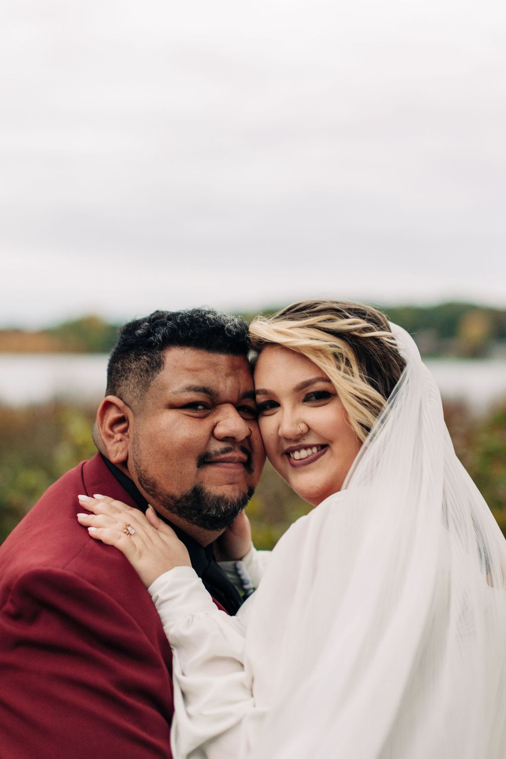 Joyful wedding portrait showing genuine laughter and happiness with lake in background.