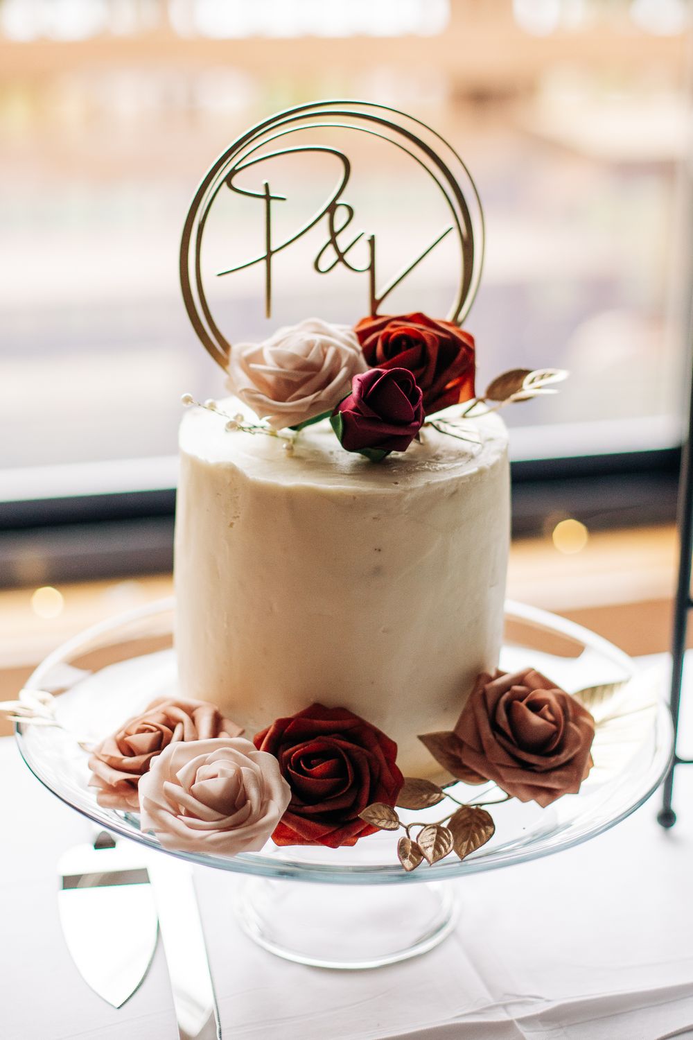 Elegant white wedding cake decorated with burgundy and blush roses and gold P&V topper.