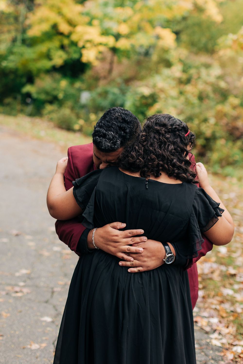 An intimate embrace captured from behind during a fall wedding photoshoot on a tree-lined path.