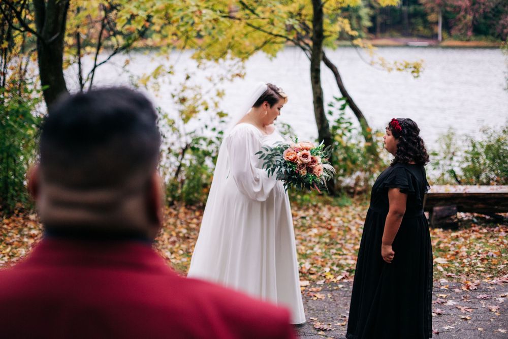 A wedding ceremony unfolds on a fall day with golden leaves and a lake in the background.