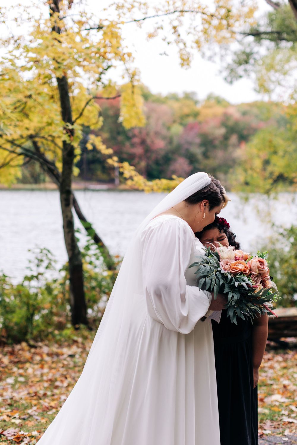 A tender moment shared during an autumn wedding ceremony beside a serene lake with golden foliage.