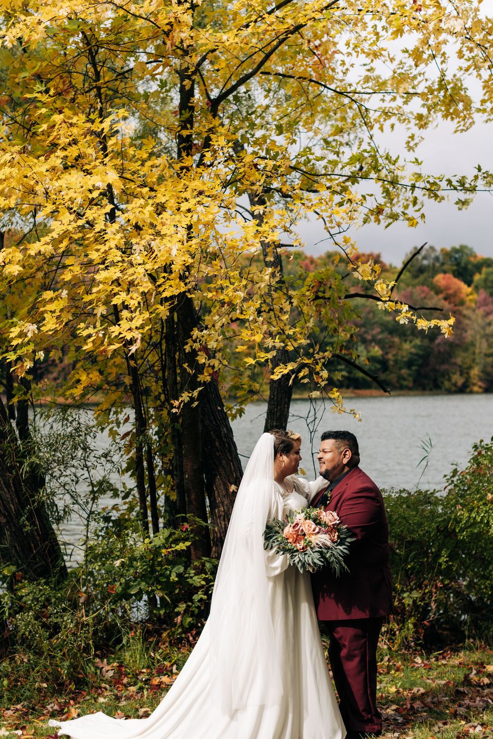 A couple shares a romantic moment under golden autumn trees beside a serene lake.