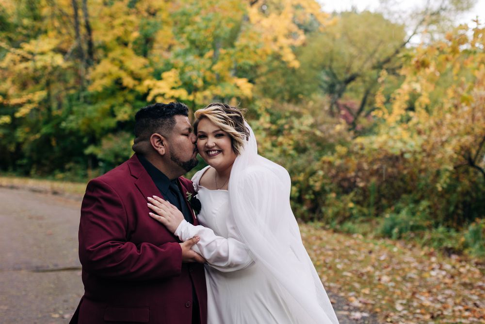 A tender moment between newlyweds on a leaf-covered path in fall.
