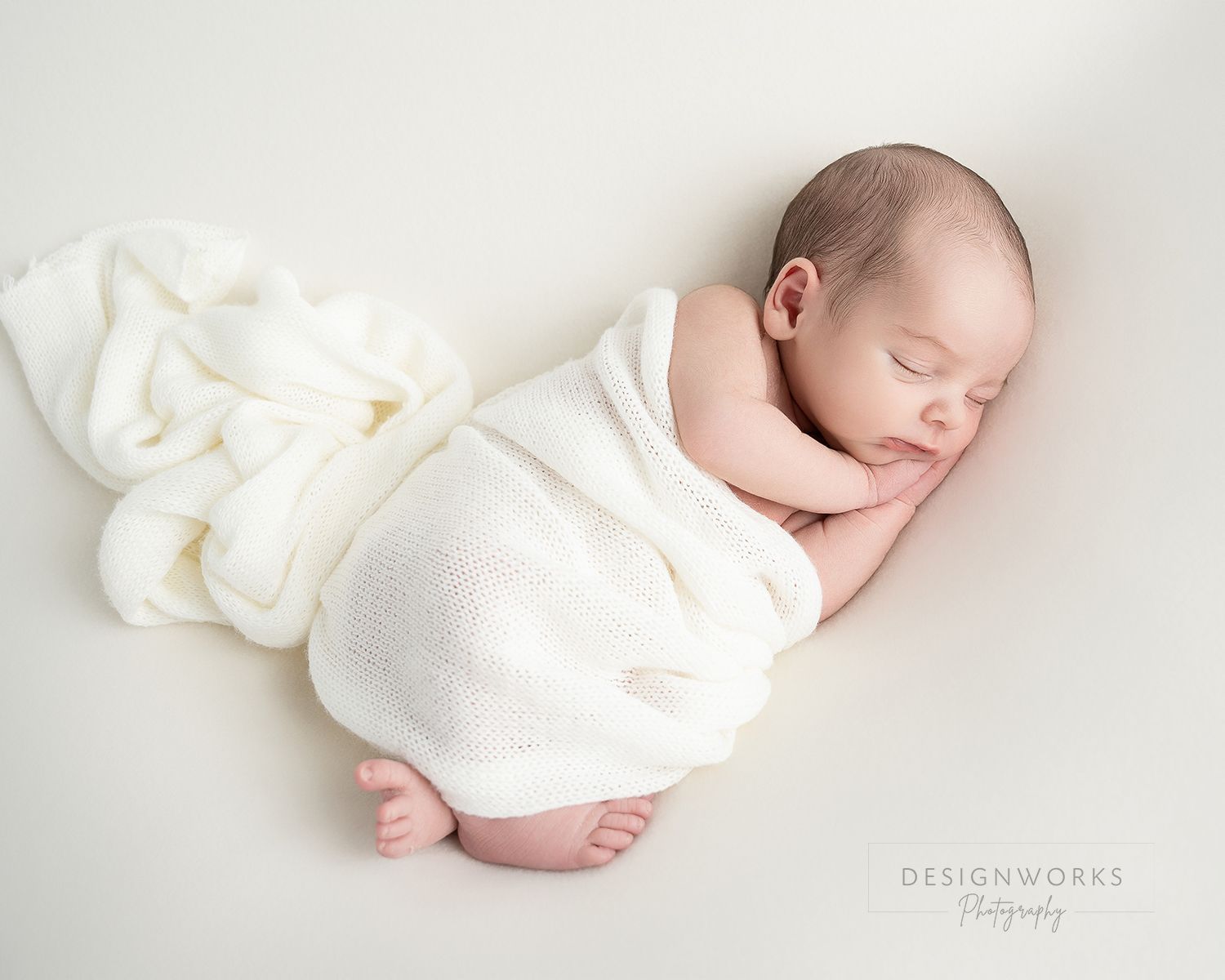 Sleeping newborn baby wrapped in white blanket on light background.