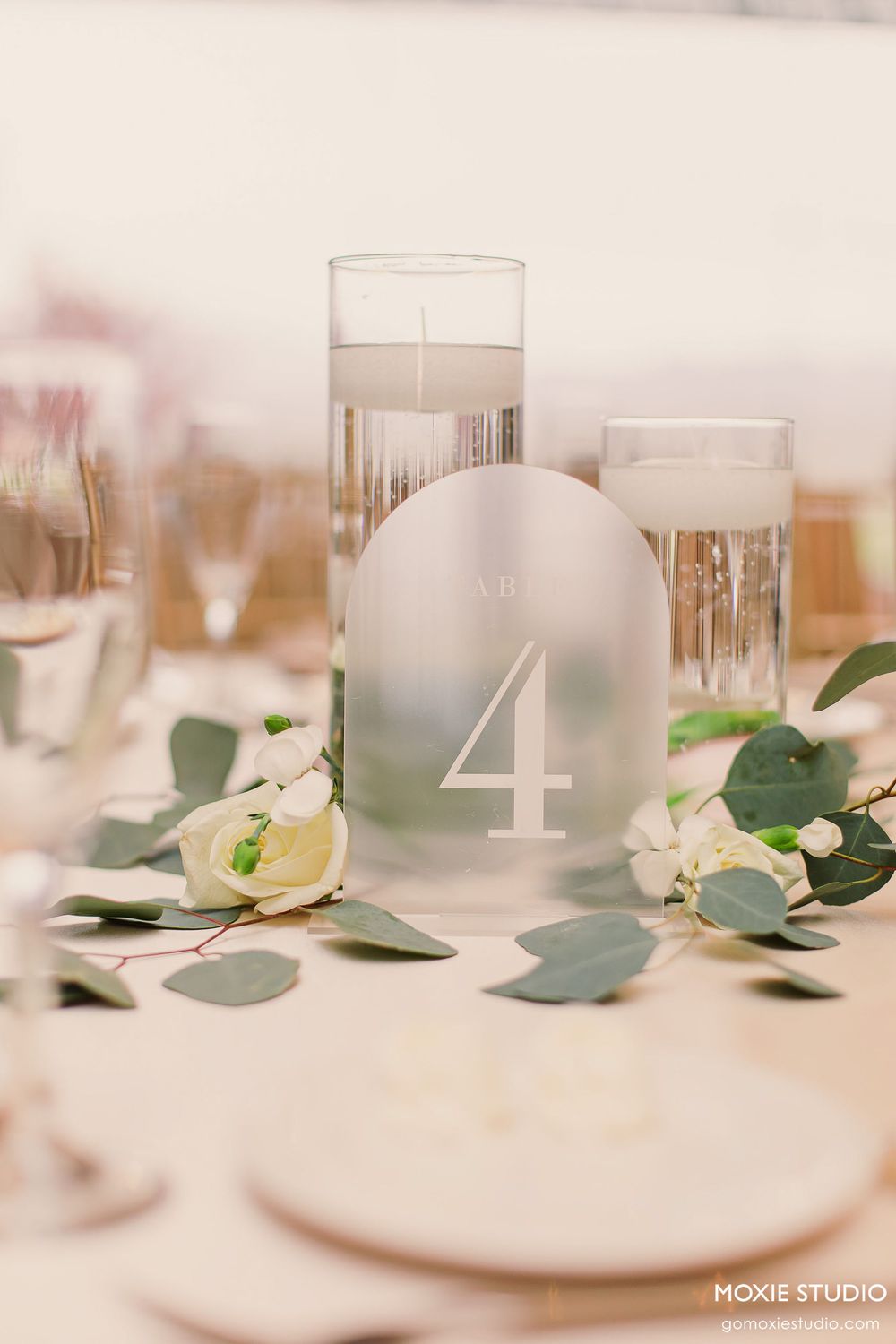 Elegant table setting with frosted glass votives and white floral arrangements on a light colored surface.