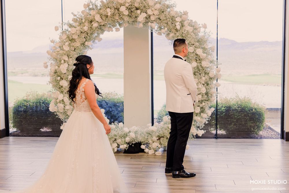 Wedding couple's first dance under an elegant floral arch with scenic views through large windows.