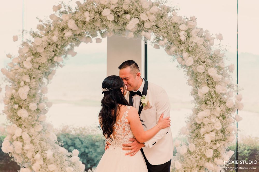A romantic wedding moment captured under a beautiful floral arch with white and blush blooms.