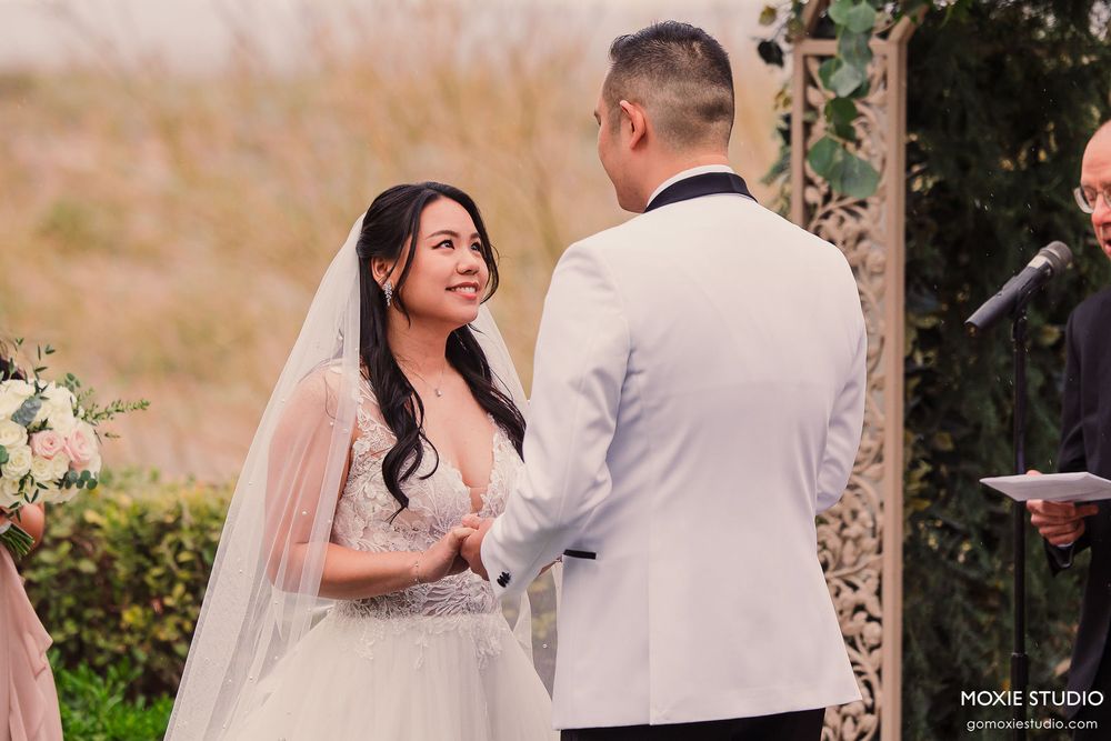 A romantic outdoor wedding ceremony with a couple exchanging vows under a floral arch in a garden setting.