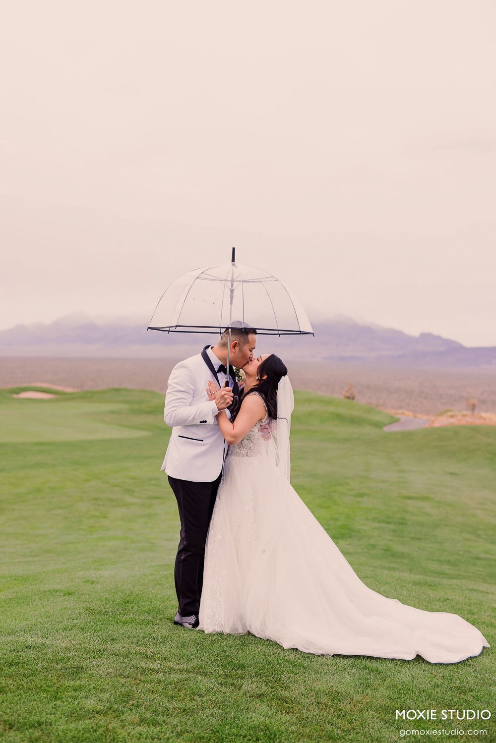 Romantic wedding photos on a golf course with mountains in the background and couple sharing umbrella.