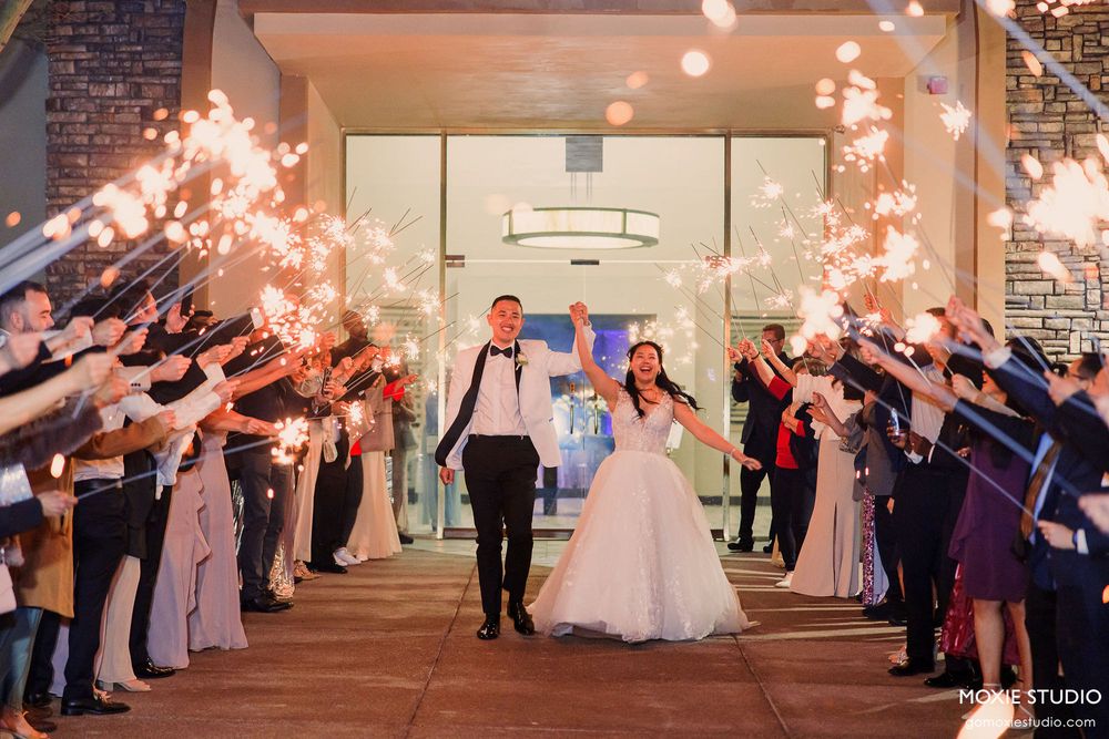Wedding guests form a sparkler tunnel exit for the newlyweds in a brick-walled venue space.