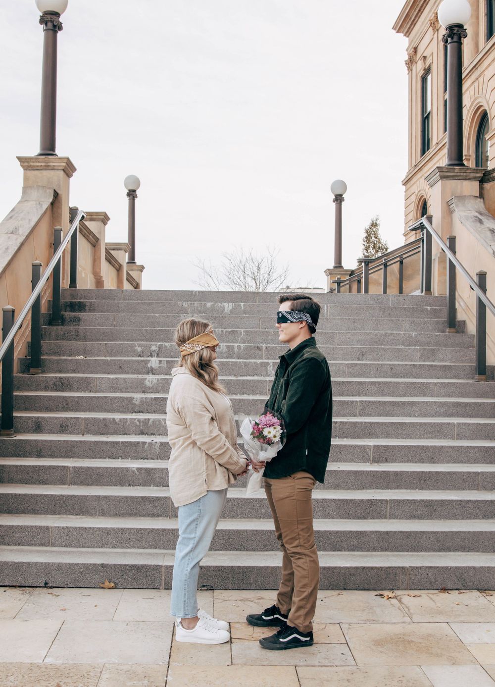 Couple holding hands on grand stone staircase of historic building.