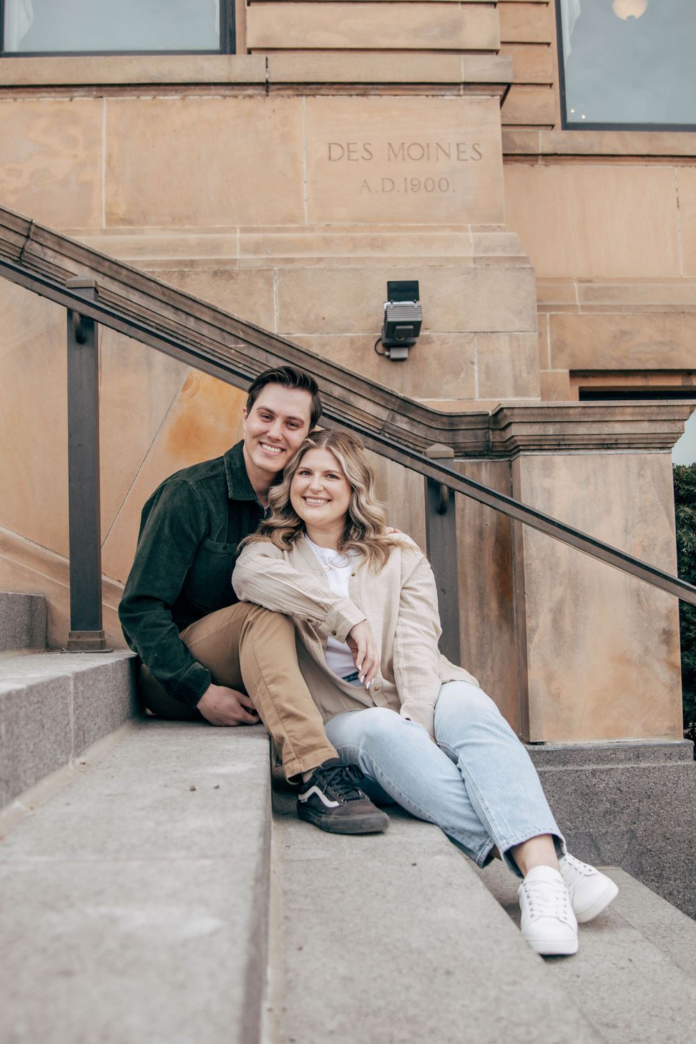 A couple sitting together on steps with 'Des Moines' visible on the building behind them.