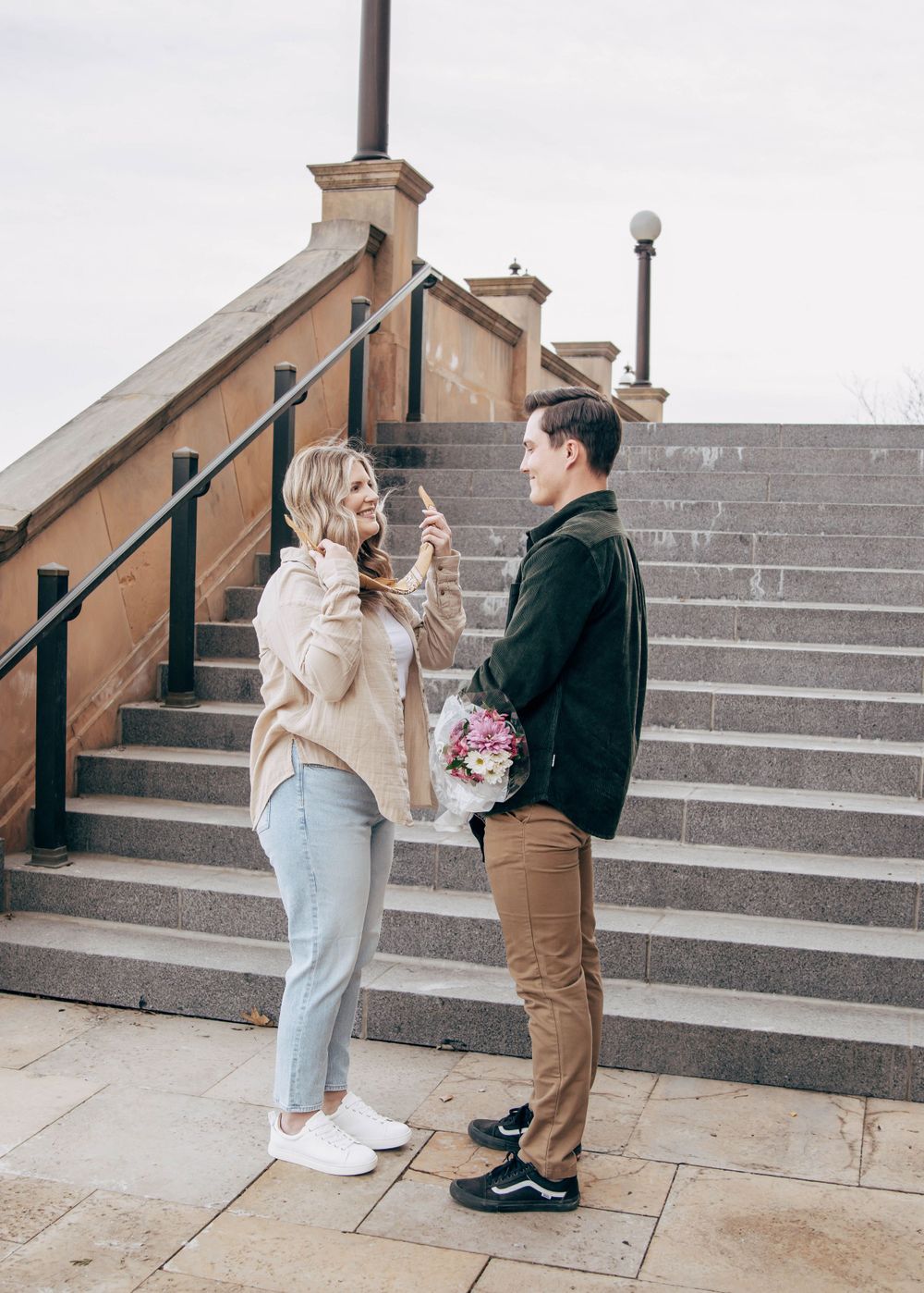 Couple sharing emotional moment on stone steps with bouquet of flowers.