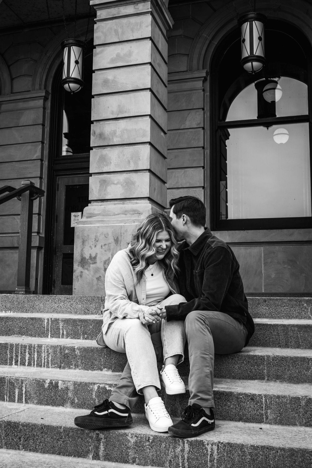 A black and white photo of a couple sitting on historic building steps.