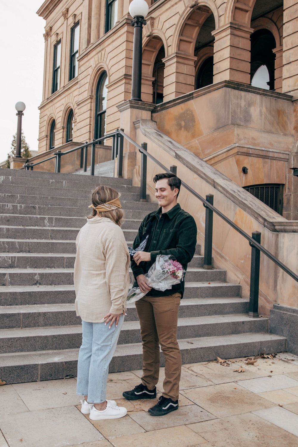Two people conversing on steps of historic building with one holding flowers.