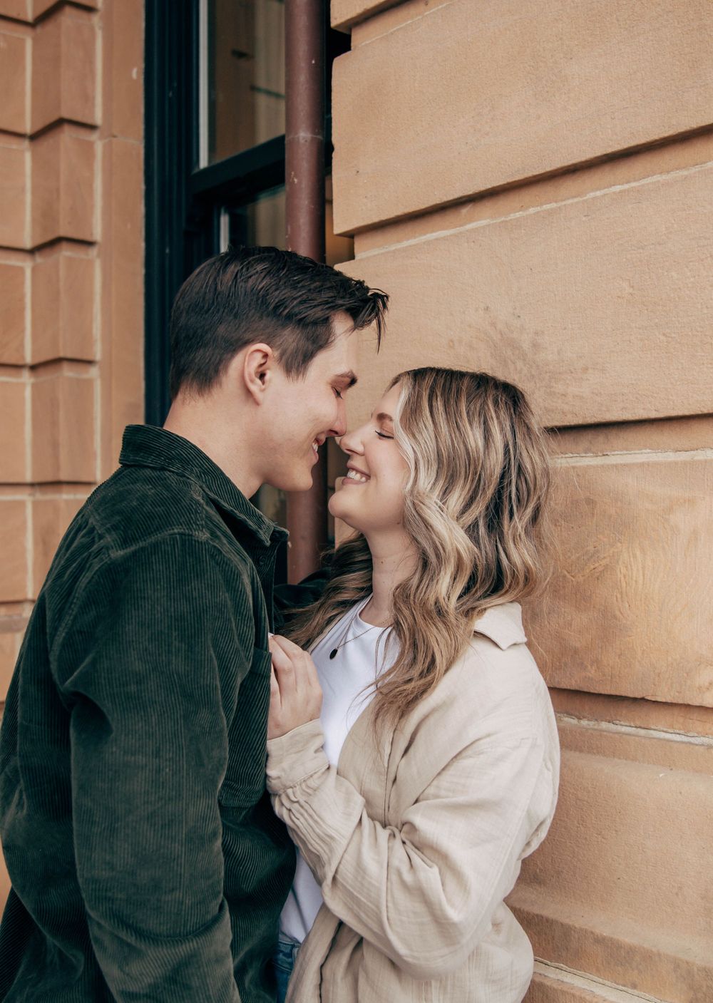 A tender moment between a couple against a beige building exterior.