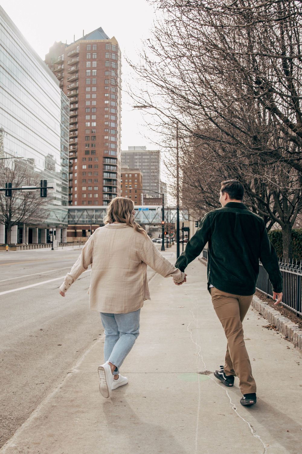 A couple holding hands while walking down an urban street with tall buildings behind them.