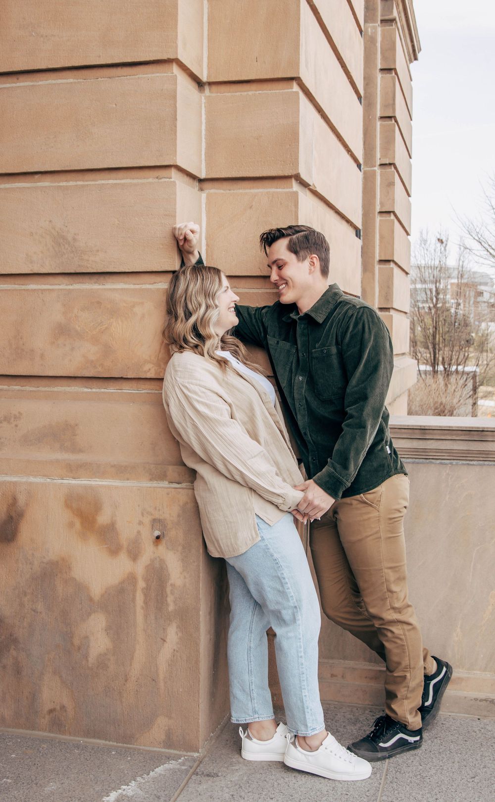 A couple sharing an intimate moment against a beige stone building wall.
