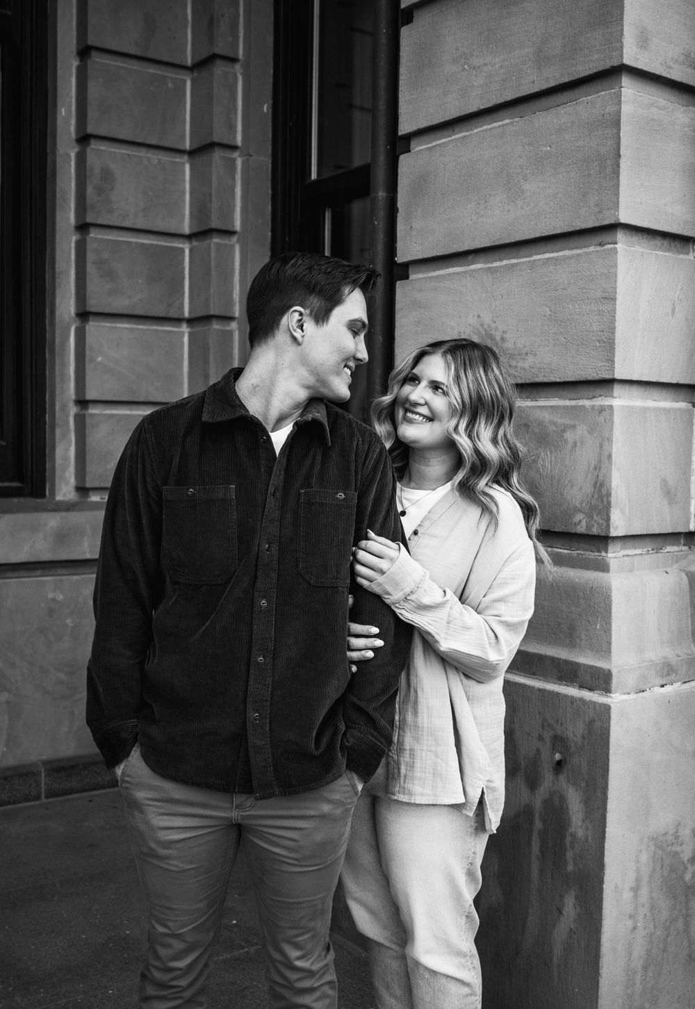 A black and white candid moment of a couple by a stone building.