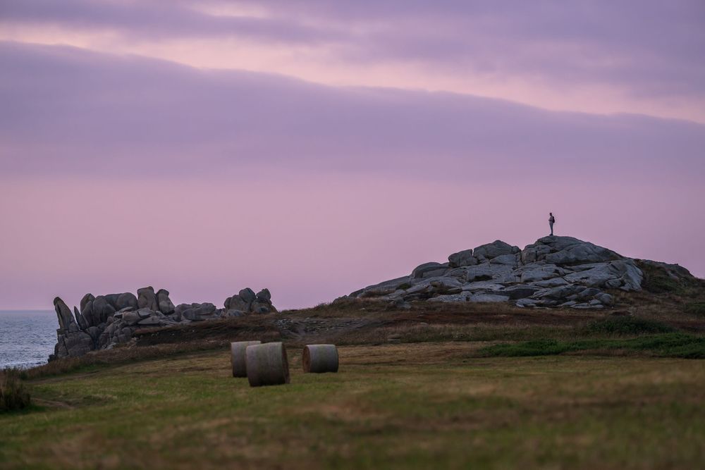 Purple twilight sky over a series of rocky coastal landscapes with distant headlands and hay bales in the fields.