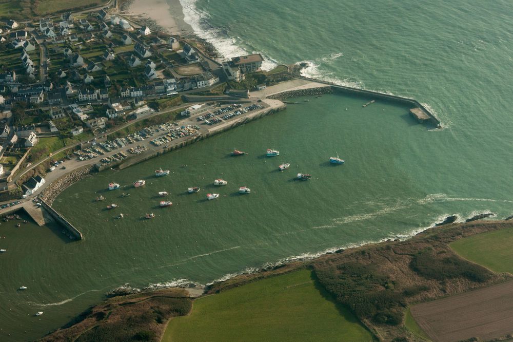 Aerial view of a coastal harbor with boats anchored in turquoise waters surrounded by green landscape.