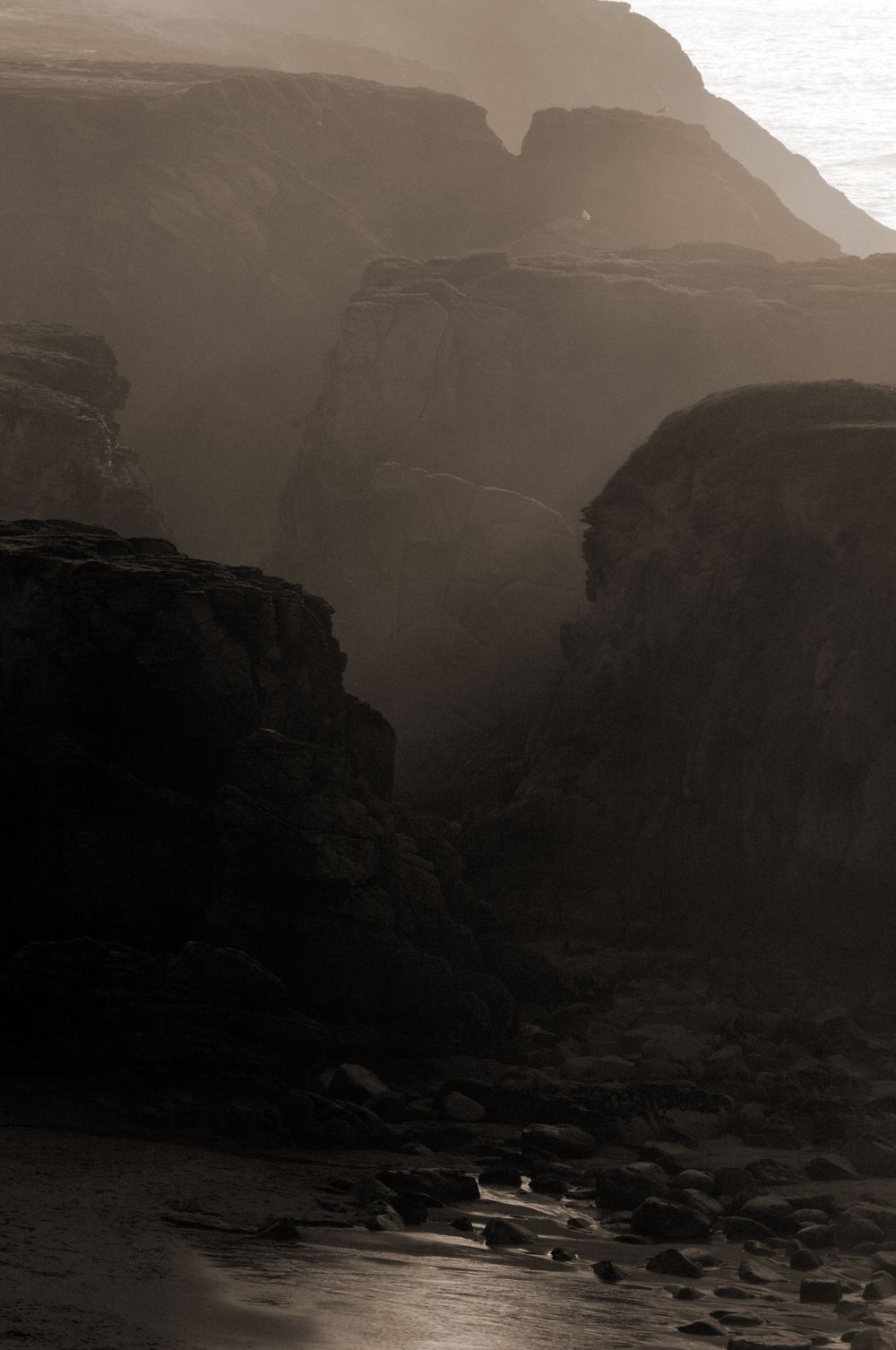 Misty canyon cliffs in sepia tones with dramatic layered rock formations.
