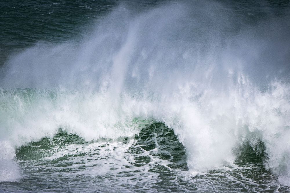 Powerful wave breaks and sprays white water against dark ocean backdrop.
