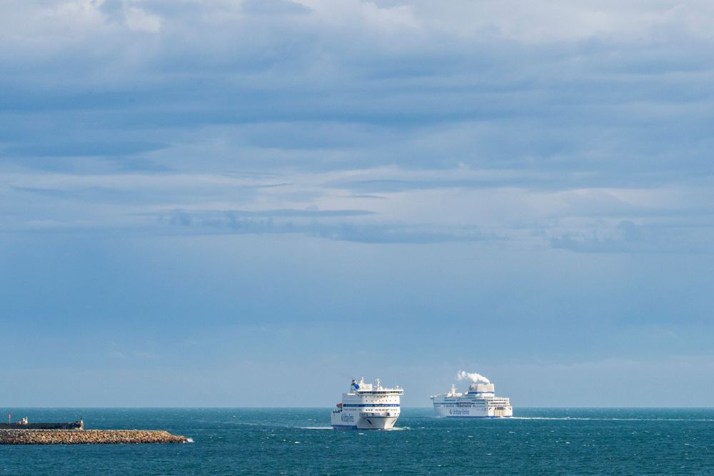 Two cruise ships sail on calm blue ocean under cloudy sky.