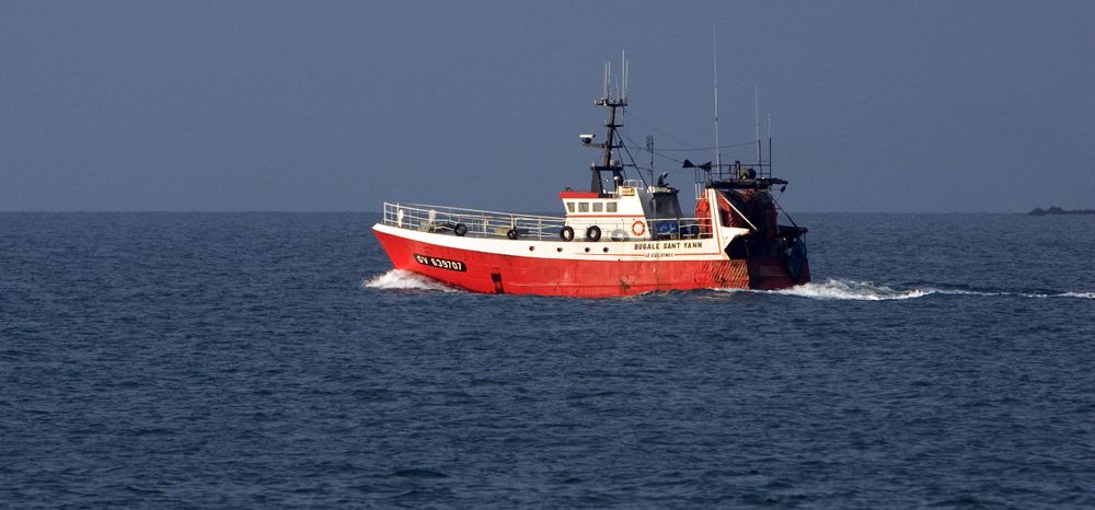 Red and white fishing vessel sailing on deep blue ocean waters.